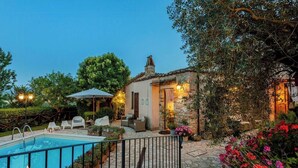 A poolside area with a stone pool, outdoor seating, and a building with stone walls and a tiled roof. - Historic village with pool near Todi (Todi)