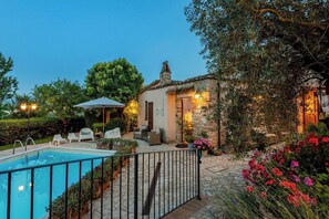Ein Poolbereich mit Steineinfassung, Gartenmöbeln und einem Gebäude mit Steinmauern und einem Ziegeldach.