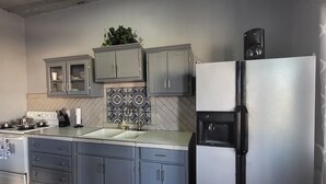 Une cuisine avec des meubles gris, un réfrigérateur en acier inoxydable, une machine à café et un dosseret carrelé.