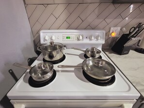 Une cuisine avec un fourneau blanc, trois casseroles sur les brûleurs et un porte-couteaux sur le plan de travail.