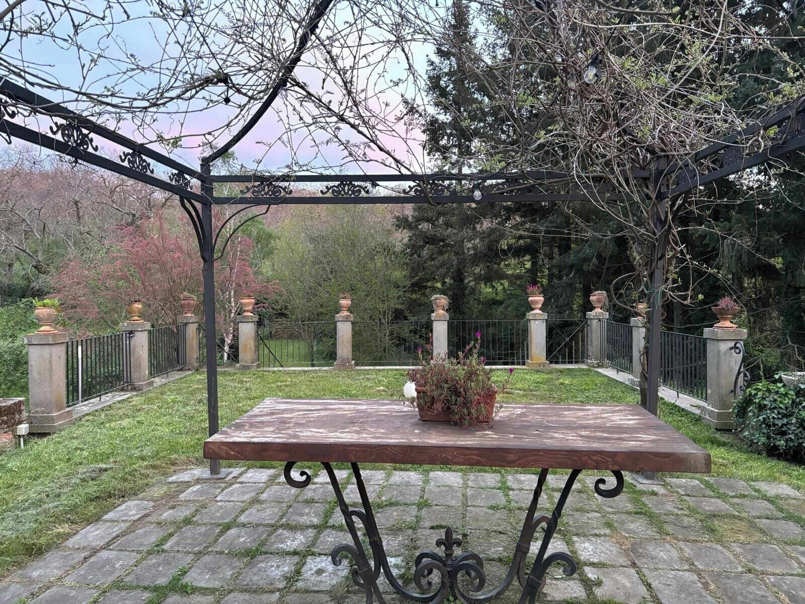 Un patio jardín con una mesa y sillas, rodeado por una cerca de hierro forjado y pilares de piedra.