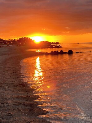 Tramonto su una spiaggia con rocce e una costa in lontananza.
