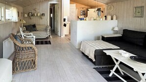 Una habitación amplia con suelo de madera, un sofá, una mesa de comedor y una silla de mimbre.