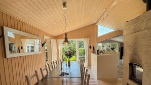 Un comedor con una larga mesa de madera, sillas, un tapete a rayas, una lámpara colgante y una chimenea de ladrillo.