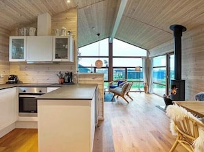 Moderni keittiö, jossa on suuri keittiösaareke, ruokailutila korkean pöydän ja tuolien kera sekä puukamiina.