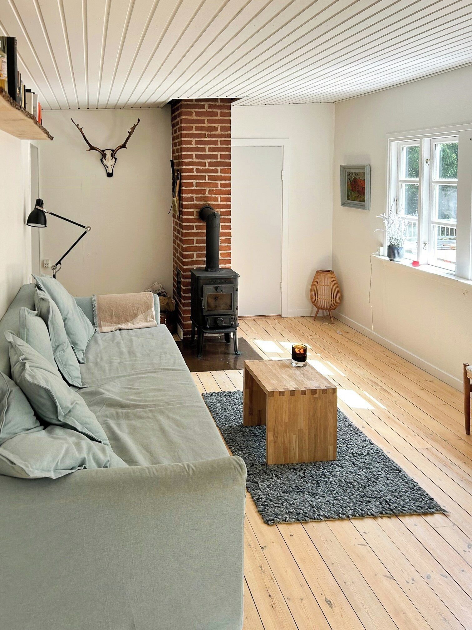 A cozy living room with a brick fireplace, a sofa, a coffee table, and a window with a view.