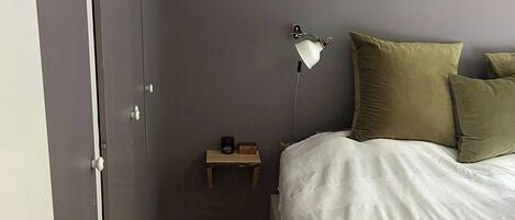 A bedroom with a bed, a nightstand, a lamp, and a door.