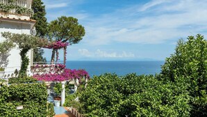 Un edificio costero con balcón, abundante vegetación y vista al mar.