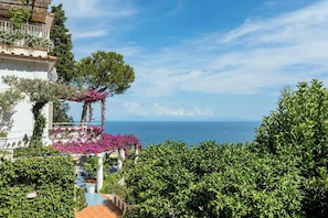 Ein Küstengebäude mit Balkon, üppiger Bepflanzung und Blick aufs Meer.