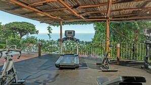 Un gimnasio al aire libre con equipo de ejercicio, una cinta de correr y vistas al mar.