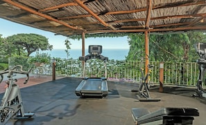 Ein Outdoor-Fitnessbereich mit Trainingsgeräten, Laufband und Meerblick.
