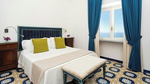 Una habitación de hotel con cama, un banco, una mesita de noche, una ventana con cortinas y suelo estampado.