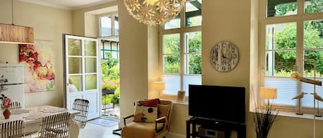 Un salon spacieux comprenant un coin repas, de grandes fenêtres, un téléviseur à écran plat et un luminaire décoratif au plafond.