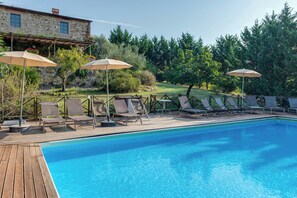 A swimming pool with lounge chairs and umbrellas, surrounded by a wooden deck and a stone building. - Rustic villa with pool in the heart of Chianti (San Casciano in Val di Pesa)