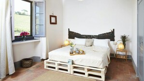 Ein Schlafzimmer mit Bett, Nachttischen, einem Fenster mit Vorhängen, einem Holz-Kopfteil und Blick ins Freie.