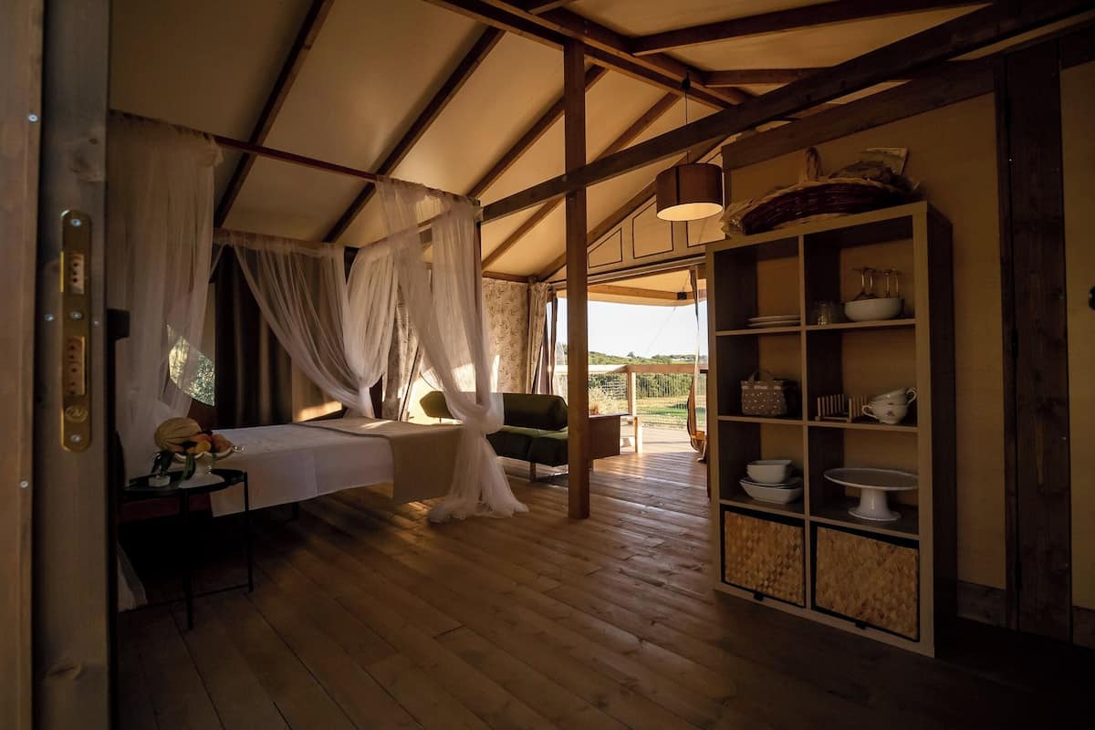 Una habitación con una cama, una mesita, una repisa con vajilla y vistas al exterior.