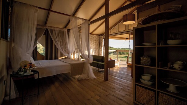 A room with a bed, a small table with a fruit bowl, a shelf with dishes, and a view of the outdoors. - Glamping Podere San Jacopo (Massa Marittima)