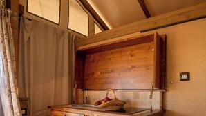 A wooden kitchen with a hanging light fixture, wooden cabinets, and a tiled backsplash. - Glamping Podere San Jacopo (Massa Marittima)