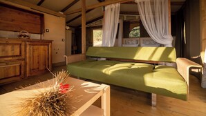 A room with a green sofa, wooden cabinets, a table with dried plants, and a canopy bed. - Glamping Podere San Jacopo (Massa Marittima)