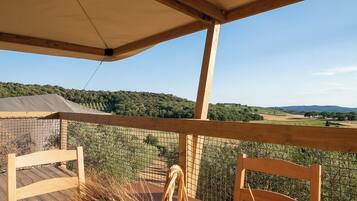 Una mesa de madera con una cesta de frutas y verduras, una silla de mimbre y vistas a un paisaje montañoso.