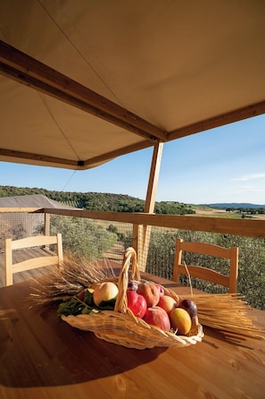A wooden table with a basket of fruits and vegetables, a wicker chair, and a view of a hilly landscape. - Glamping Podere San Jacopo (Massa Marittima)