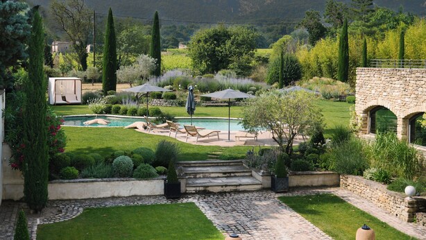 Un jardín ajardinado con piscina, mobiliario exterior y un muro de piedra.