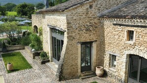 Un edificio de piedra con patio, ventanas amplias y piscina.
