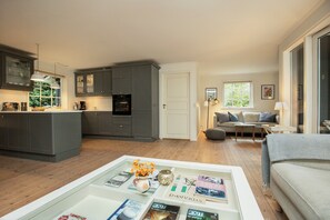 A modern kitchen with grey cabinets, a dining area with a white table, and a living room with a grey sofa. - Holiday home with wildlife near Marielyst beach (Idestrup)