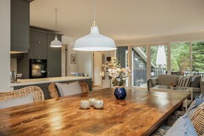A modern kitchen with dark cabinets, a dining area with a wooden table, wicker chairs, and a blue vase with flowers. - Holiday home with wildlife near Marielyst beach (Idestrup)