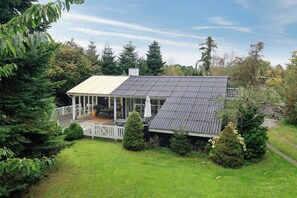 A house with a covered porch, a fenced yard, and a variety of trees. - Holiday home with wildlife near Marielyst beach (Idestrup)