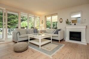 A living room with a sofa, coffee table, ottoman, fireplace, and large windows. - Holiday home with wildlife near Marielyst beach (Idestrup)
