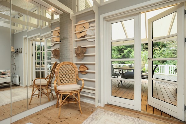 A room with a large mirror, wicker chairs, a brick wall, and a view of an outdoor deck. - Holiday home with wildlife near Marielyst beach (Idestrup)