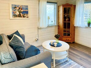 Ein Wohnzimmer mit einer Couch, einem runden Tisch mit einer Vase, einer Holzkommode und einem Gemälde an der Wand.