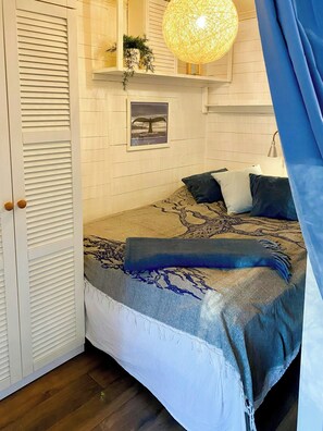 A bedroom with a bed, a hanging light fixture, a framed picture on the wall, and a closed door. - Cottage by the sea on Djurö (Djurhamn)