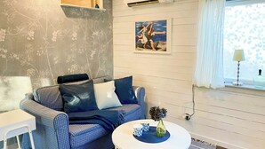 Una habitació amb un sofà estampat de quadres, una taula auxiliar blanca, una taula de centre rodona amb objectes decoratius, un quadre a la paret i una finestra amb cortina.