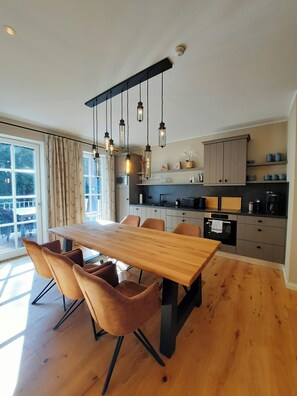 Eine moderne Küche mit einem Holzespeisetisch und Stühlen, einem eingebauten Backofen und einem großen Fenster mit Vorhängen.