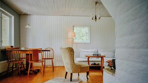 A cozy room with wooden flooring, a dining table with chairs, a patterned armchair, a white sofa, and a small side table. - Rustic cottage for creative souls by Lake Lingbo (Lingbo)