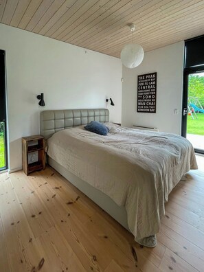 Ein Schlafzimmer mit einem großen Bett, einem Nachttisch, einer Wandlampe und Blick ins Freie.