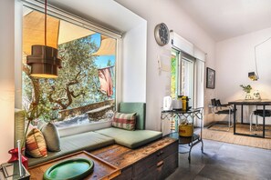 Ein moderner Wohnraum mit großem Fenster, einer Couch mit Kissen, einem Holztisch und einer Küchenzeile mit Esstisch und Stühlen.