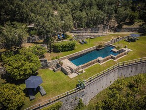 Ein Schwimmbecken, umgeben von Steinmauern, mit einer Rasenfläche und Bäumen im Hintergrund.