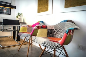 Ein modernes Interieur mit einem schwarzen Metallstuhl, einem farbenfrohen gewebten Sofa und einem Esstisch.