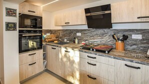 Eine moderne Küche mit Holzausstattung, einem schwarzen Backofen, einer Mikrowelle, einer Spüle aus Edelstahl und einer Marmor-Spritzschutzwand.
