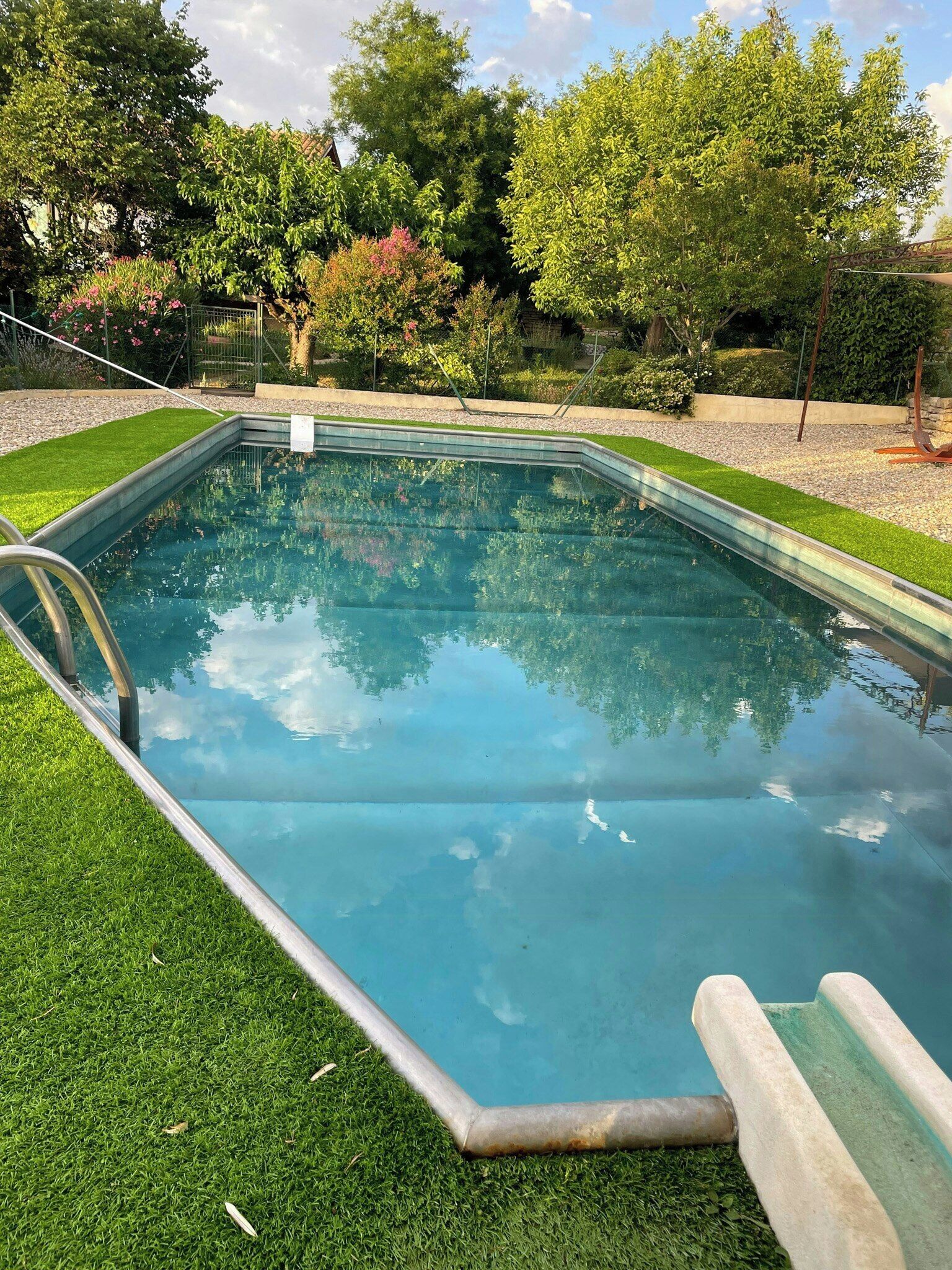 Une piscine rectangulaire à l’eau d’un bleu limpide, entourée d’une pelouse bien entretenue et de divers arbres.