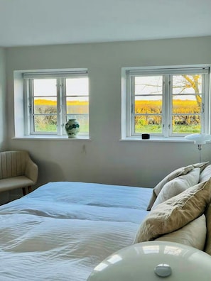 A bedroom with a bed, two windows, a chair, and a vase on the windowsill. - Historic gatehouse at Søllestedgaard Manor (Søllested)