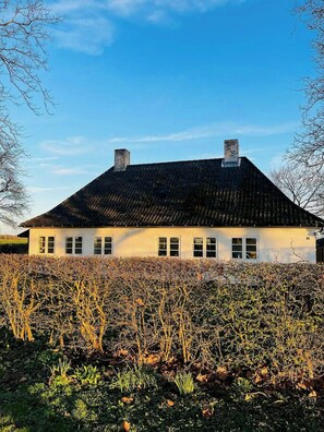 A white building with a dark roof, multiple windows, and two chimneys. - Historic gatehouse at Søllestedgaard Manor (Søllested)