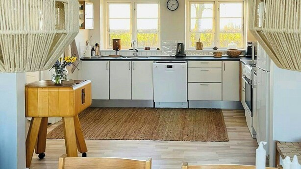 A modern kitchen with white cabinets, a wooden dining table, and a large window. - Historic gatehouse at Søllestedgaard Manor (Søllested)