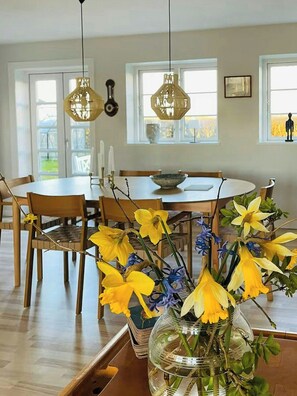 A dining area with a round table, chairs, hanging pendant lights, and a vase with flowers. - Historic gatehouse at Søllestedgaard Manor (Søllested)