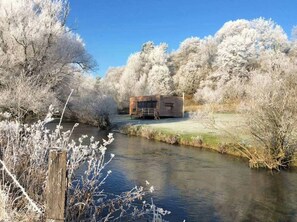 Ein rustikales Blockhaus an einem Fluss, umgeben von mit Reif bedeckten Bäumen.