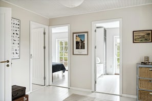 Een kamer met een bed, een deur naar een andere kamer, een lijst met een foto aan de muur, en een tafeltje met een lamp.