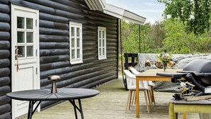 A log cabin with a porch, a round table, chairs, and a grill.